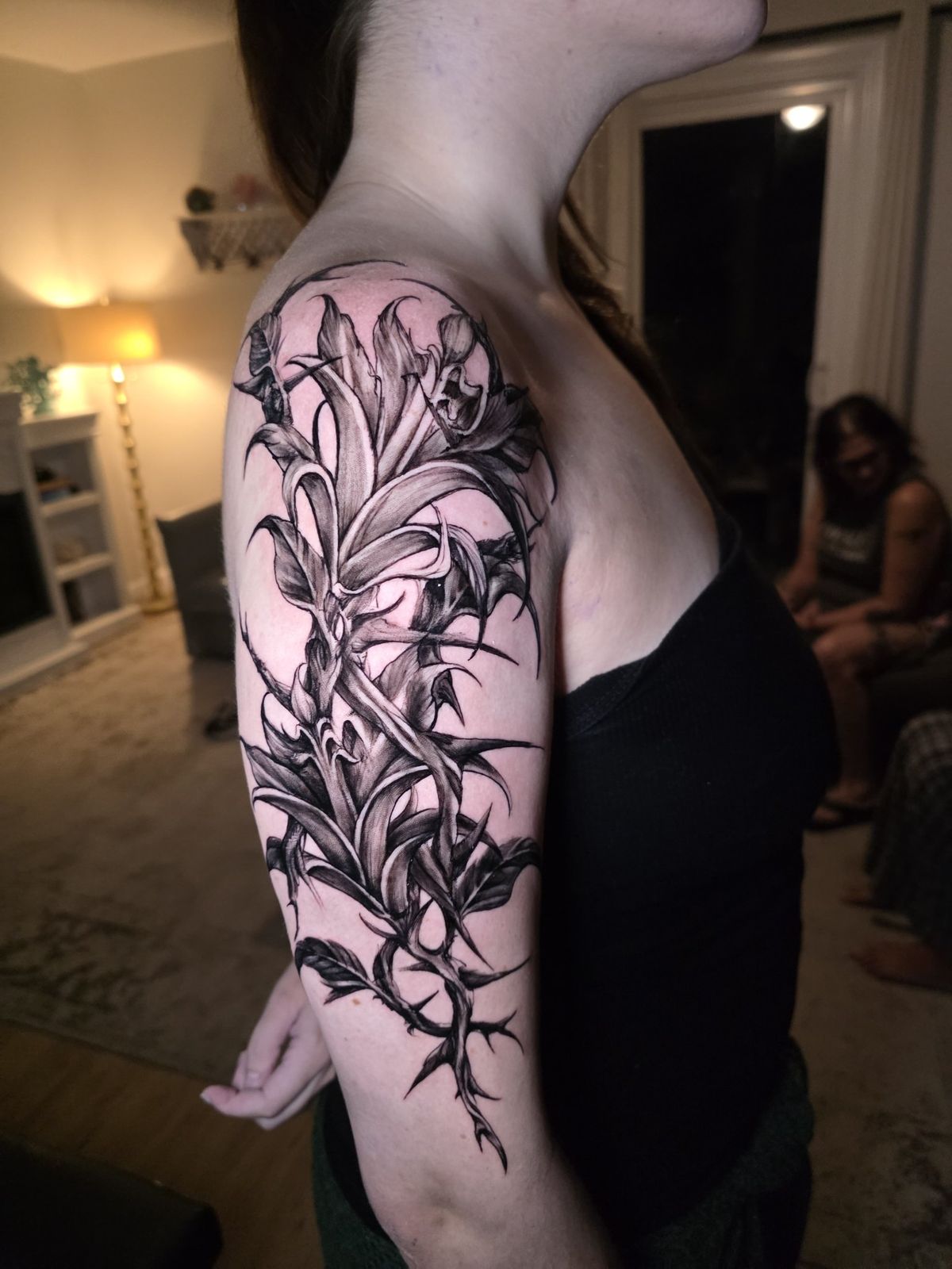 Dark botanical black-and-gray tattoo wrapping the upper arm