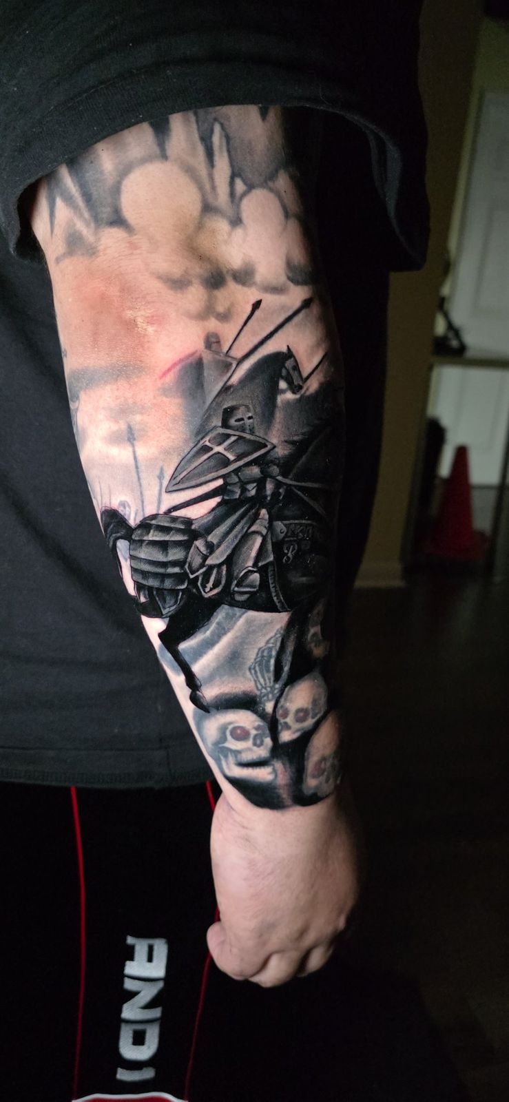 Side view of a detailed knight, horse and skulls forearm tattoo