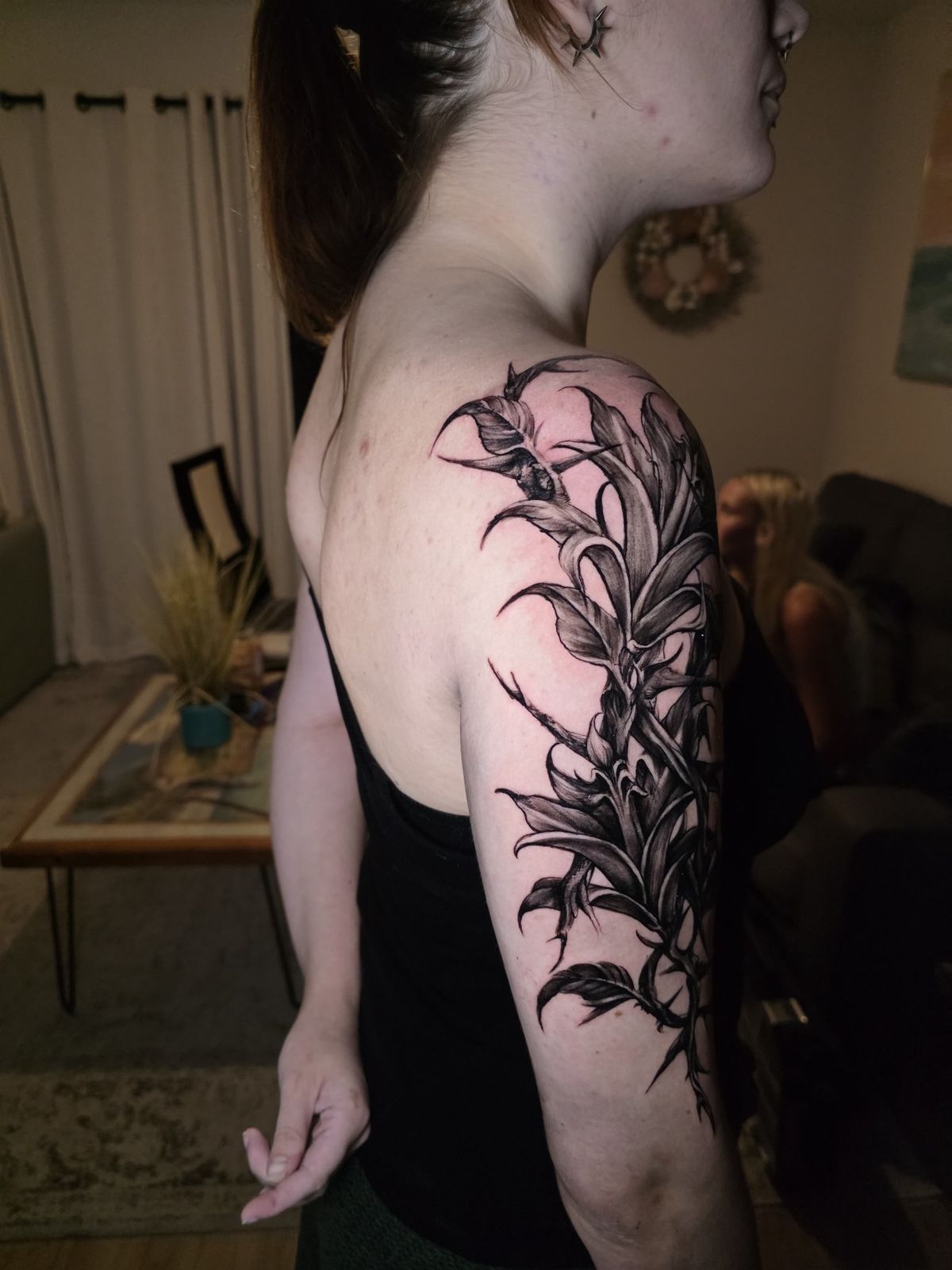 Blackwork botanical tattoo with pointed leaves wrapping the upper arm and shoulder