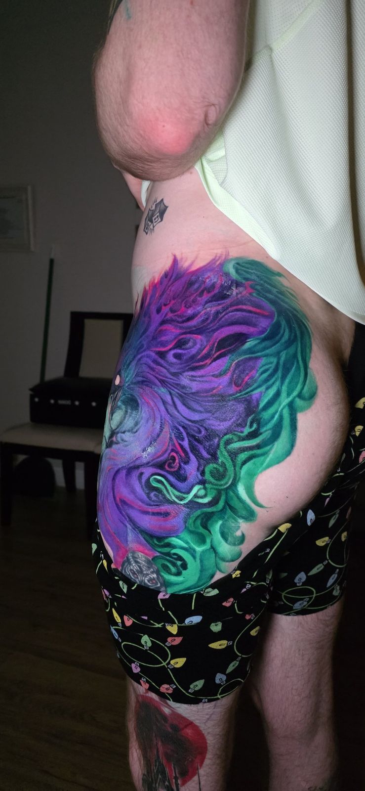 Side view of a vivid purple, teal and magenta phoenix tattoo across the thigh