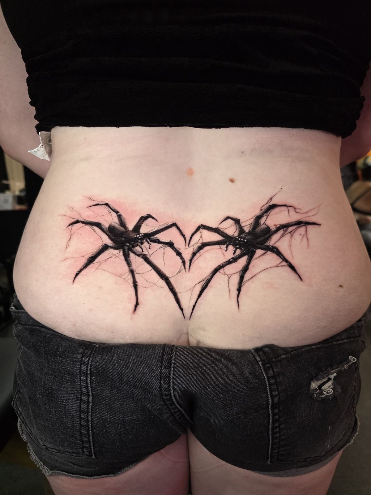 Mirrored black spider tattoos spanning the lower back
