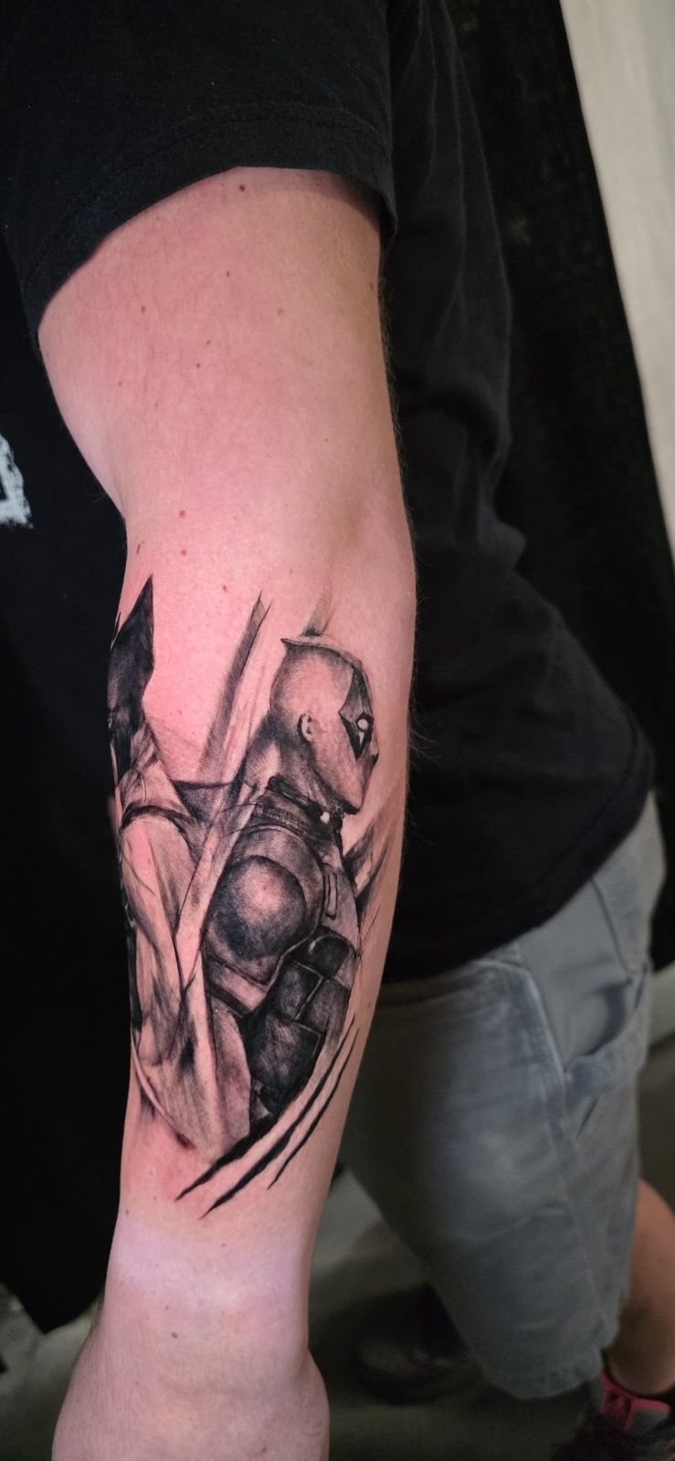 Black-and-gray armored figure tattoo with sweeping blade-like shapes on the forearm