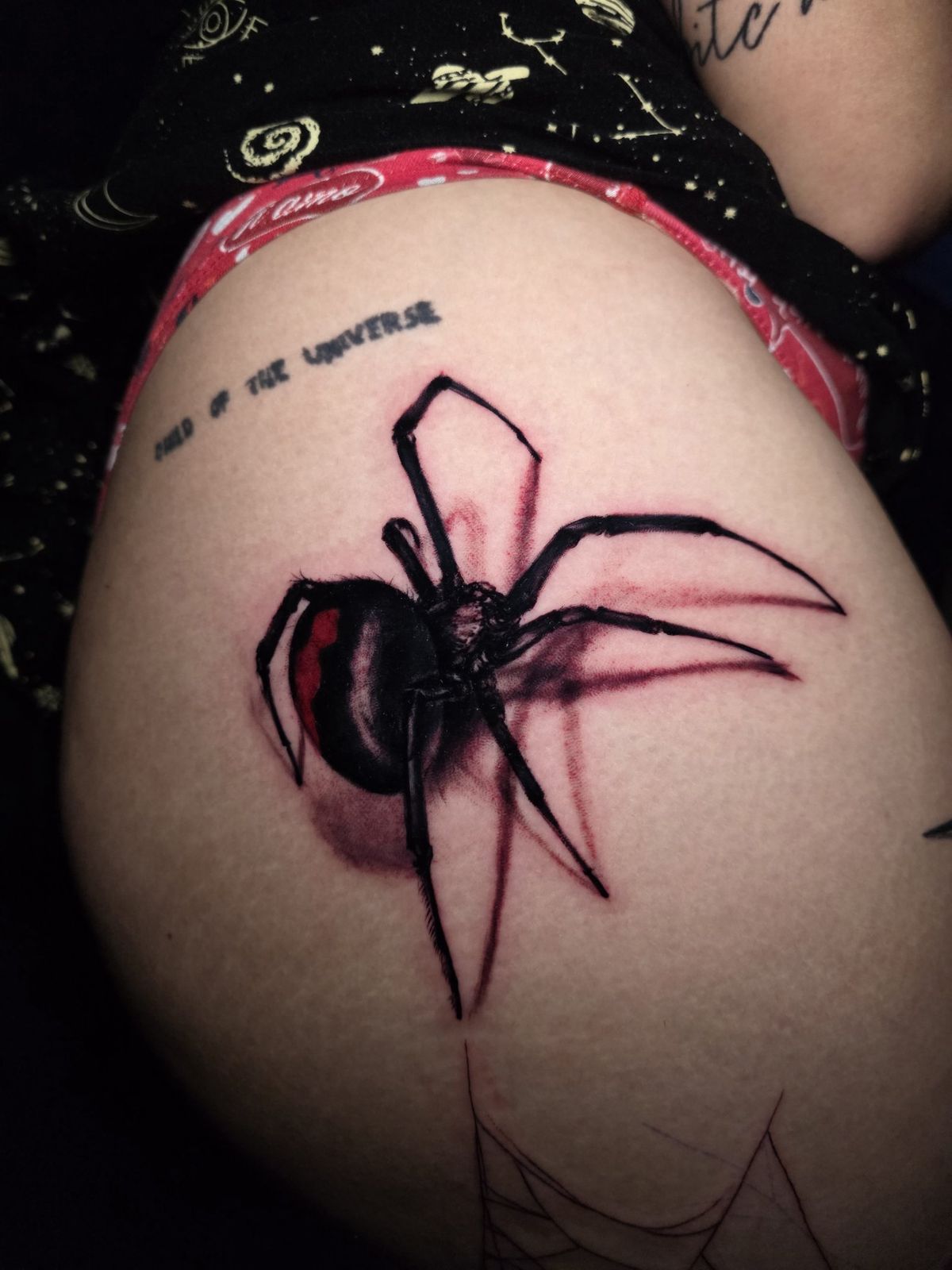 Black widow thigh tattoo with red accents and Child of the Universe script