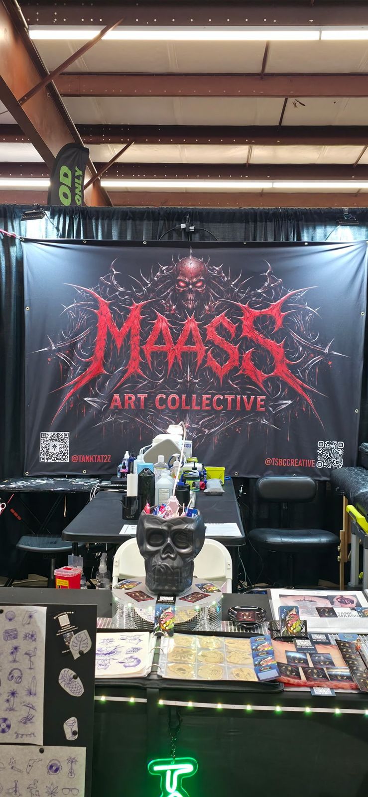Maass Art Collective convention booth with banner, artwork and tattoo setup