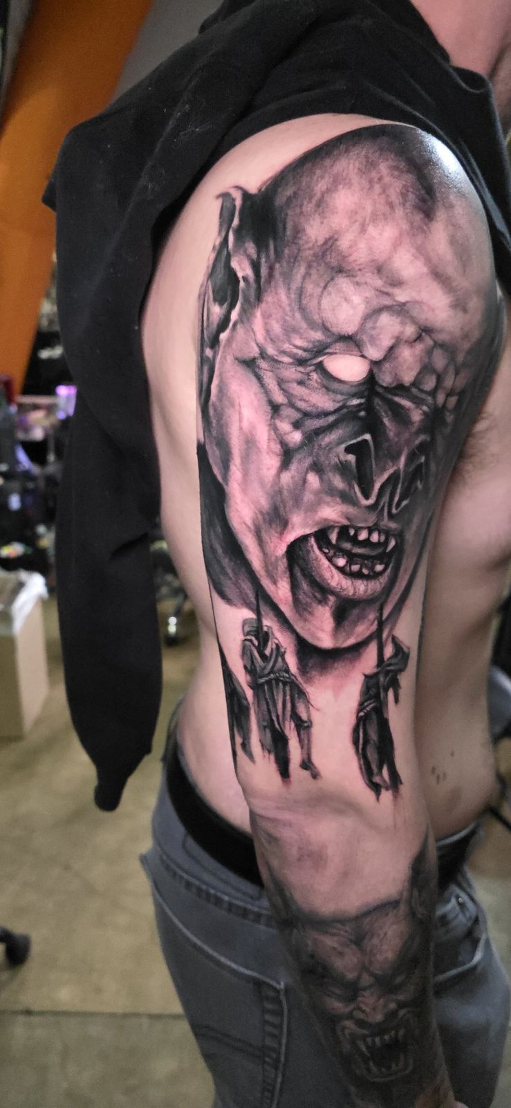 Large black-and-gray horror portrait tattoo on the upper arm