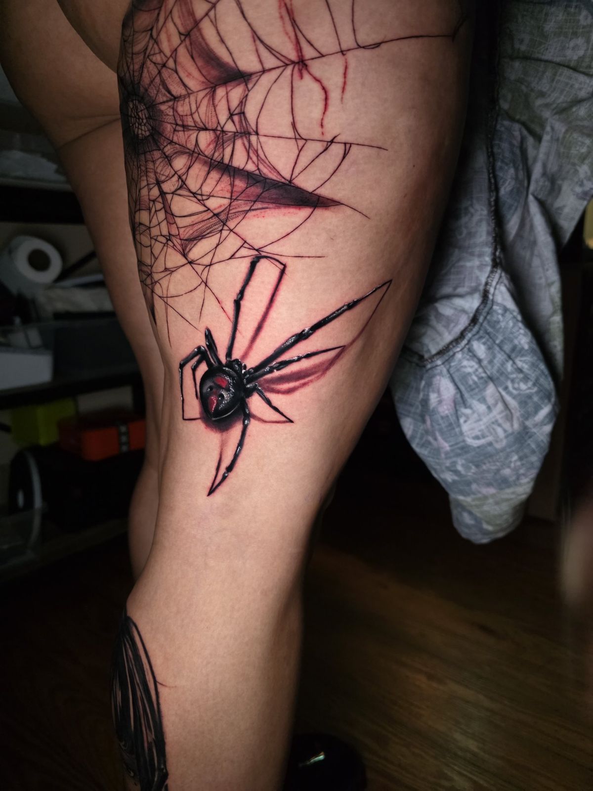 Black widow spider and web tattoo shown along the leg