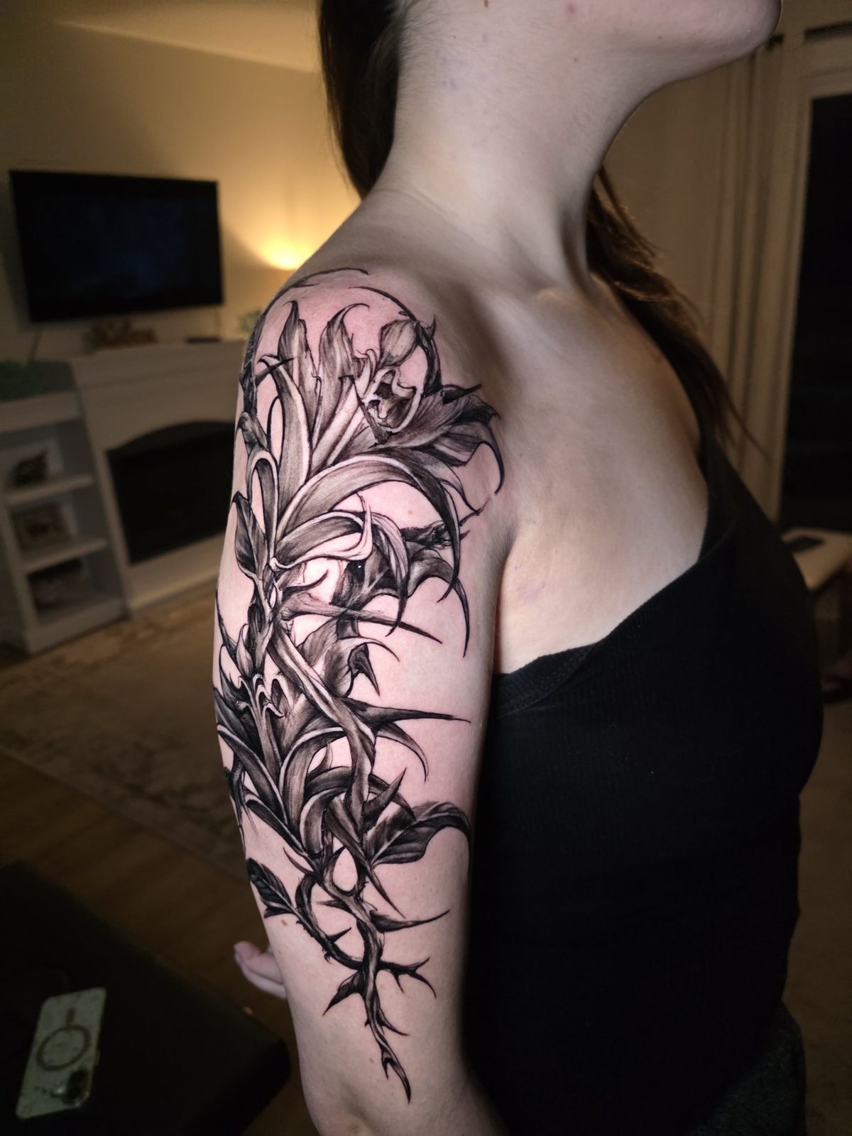 Side view of a blackwork botanical tattoo flowing from shoulder to upper arm