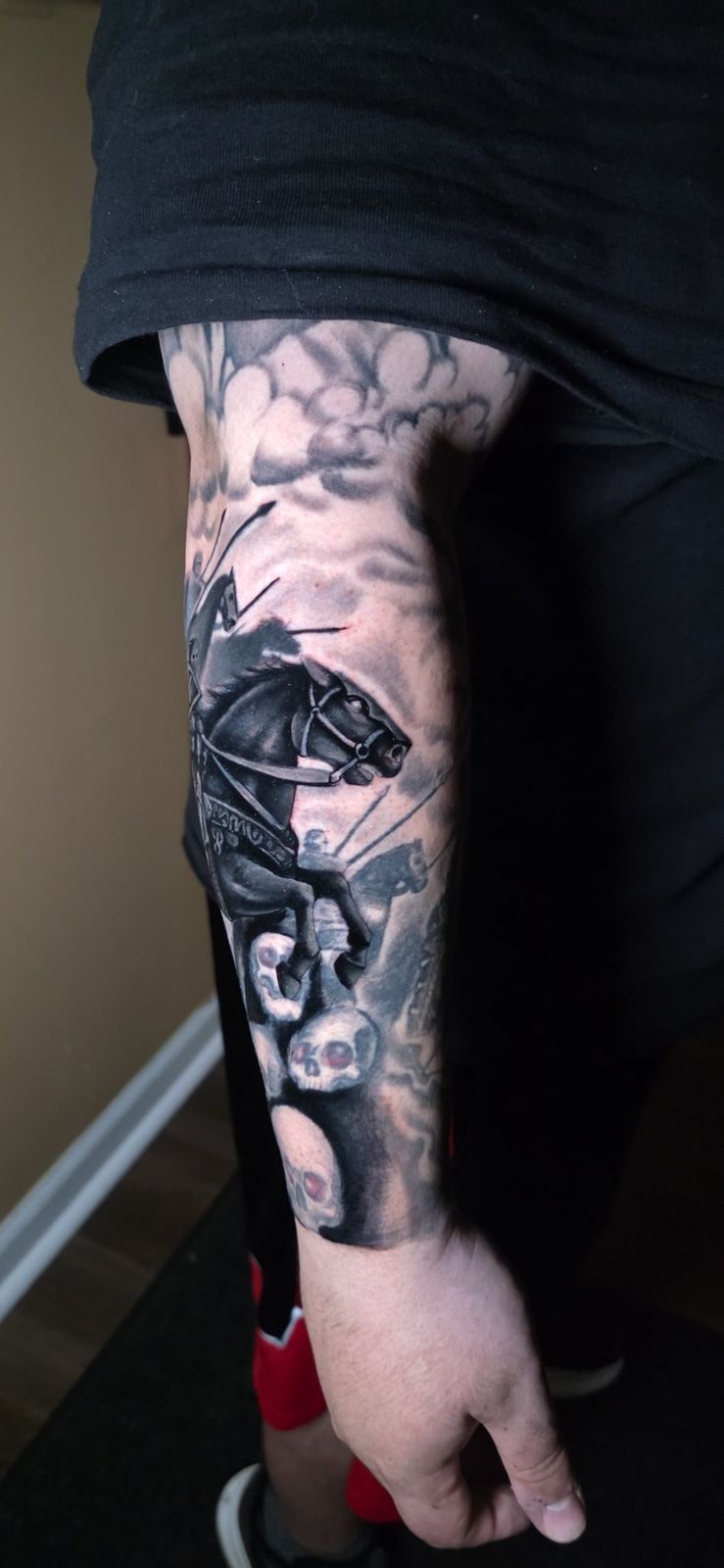 Black-and-gray knight on horseback riding above skulls on the forearm