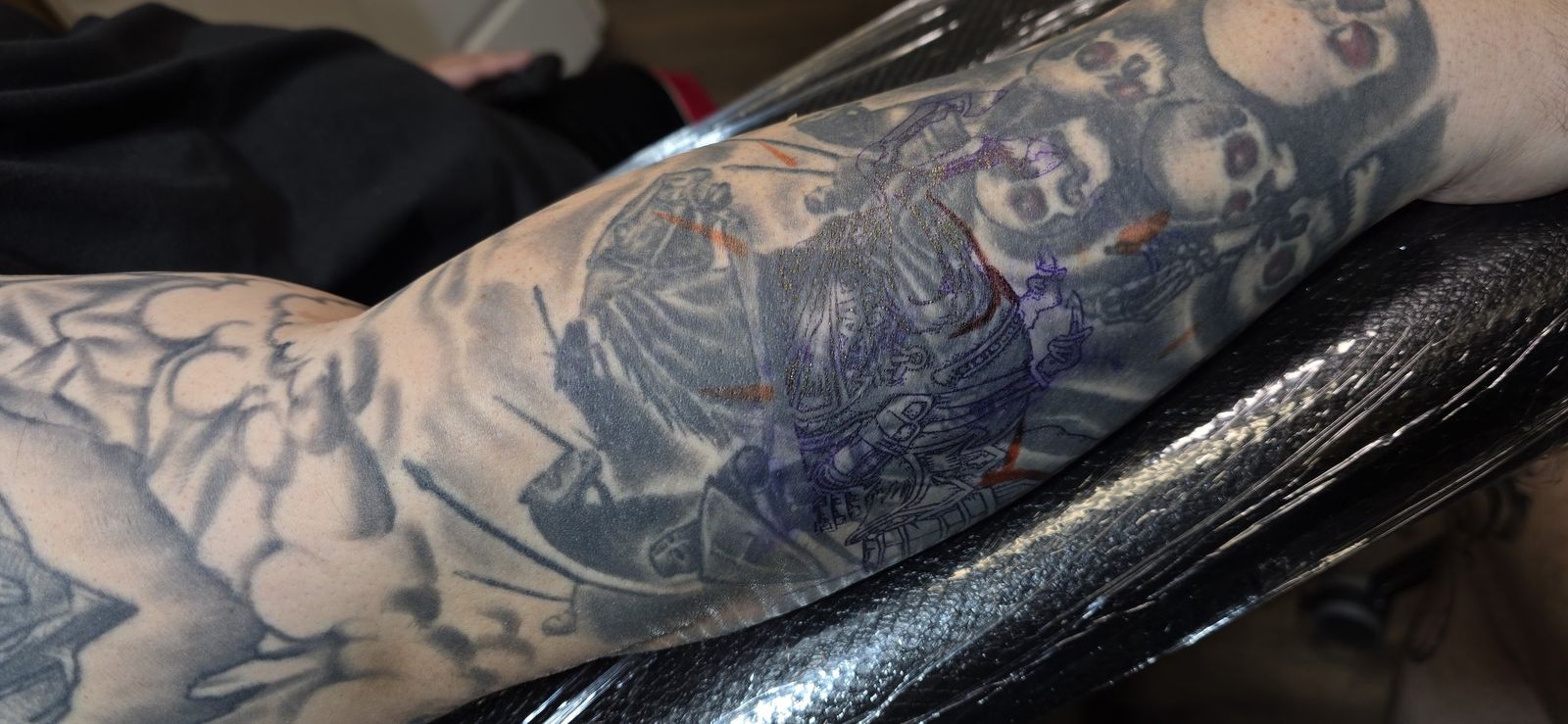 Wide view of an in-progress black-and-gray skull sleeve on the forearm