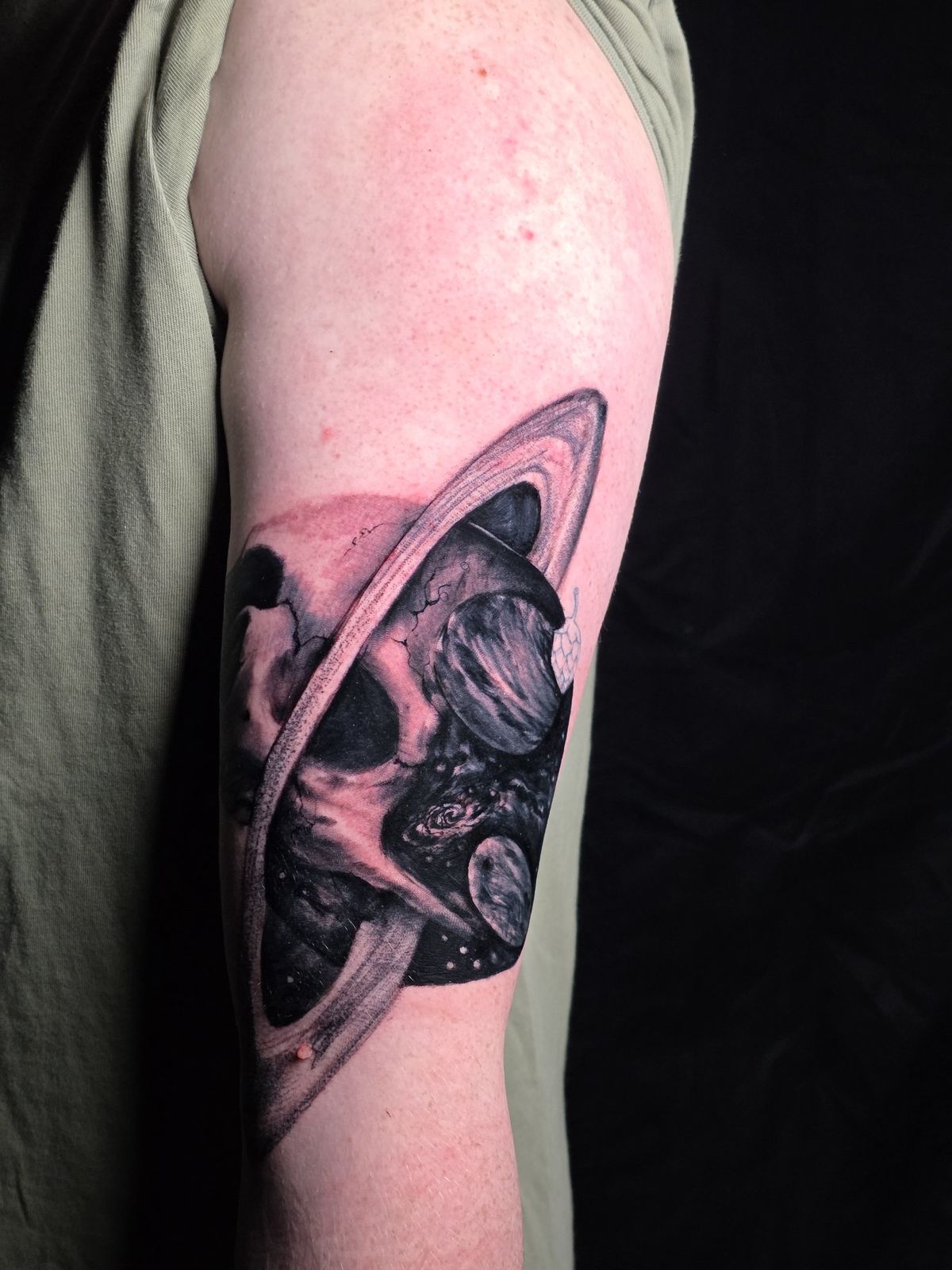 Side view of a black-and-gray skull beneath a ringed planet on the forearm