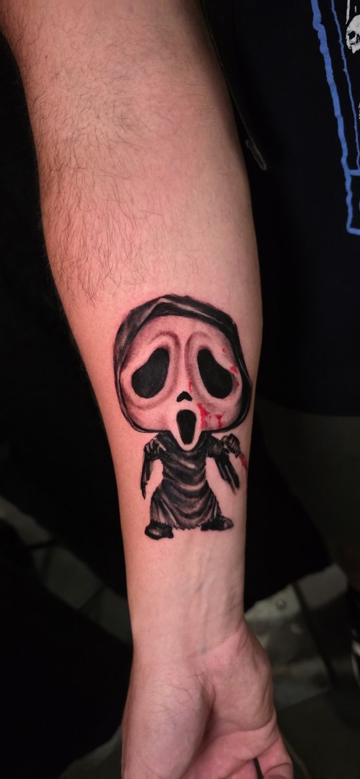 Close view of a hooded horror character tattoo with black shading and red accents