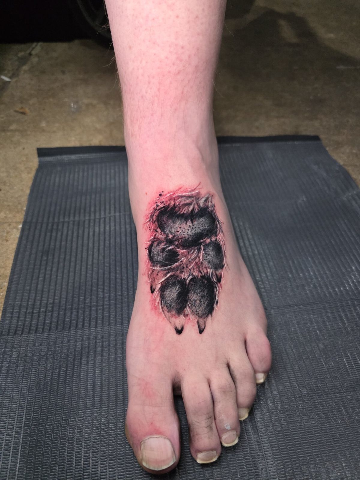 Black paw print tattoo on the top of the foot