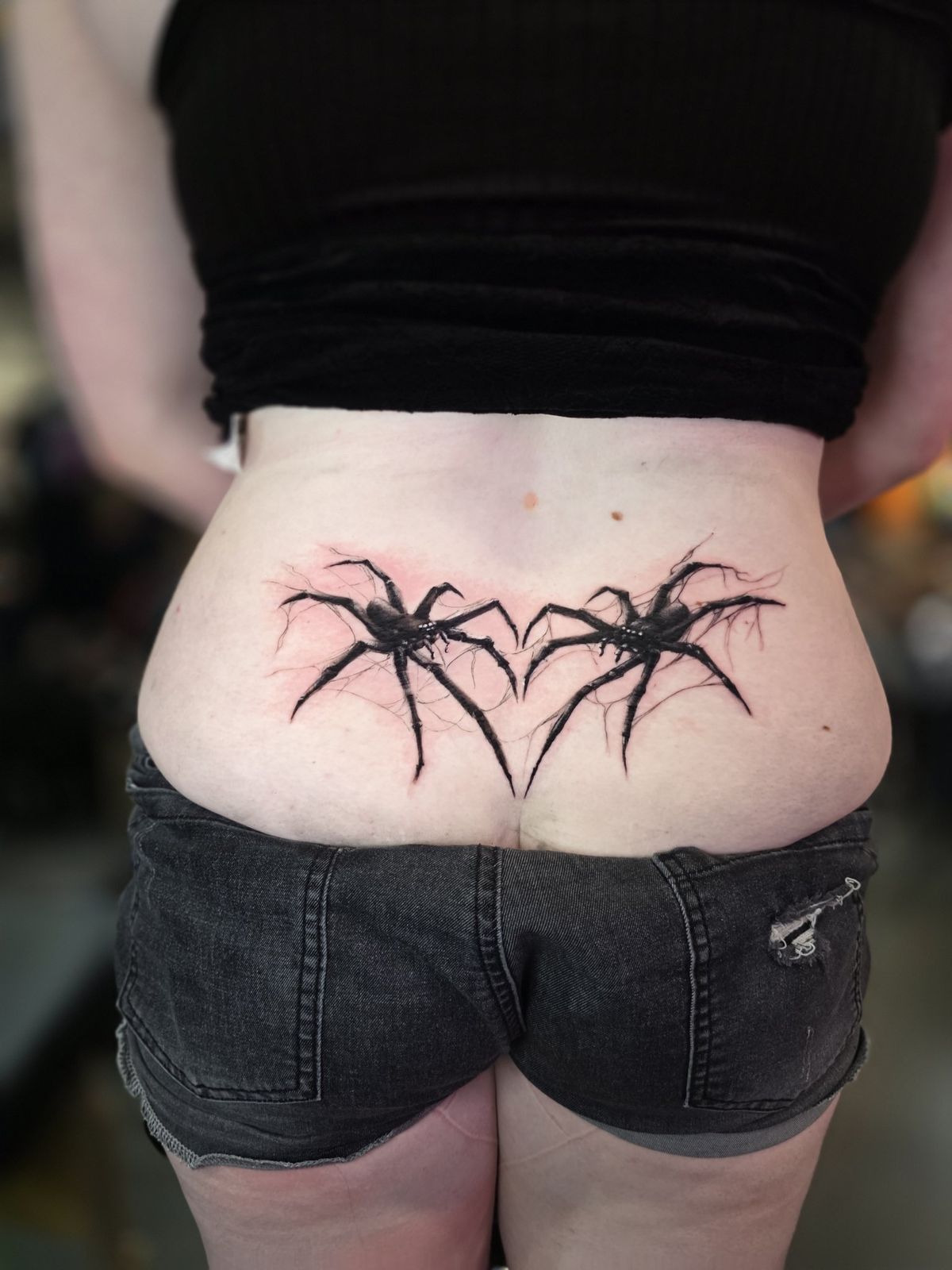 Wide view of symmetrical mirrored spider tattoos across the lower back