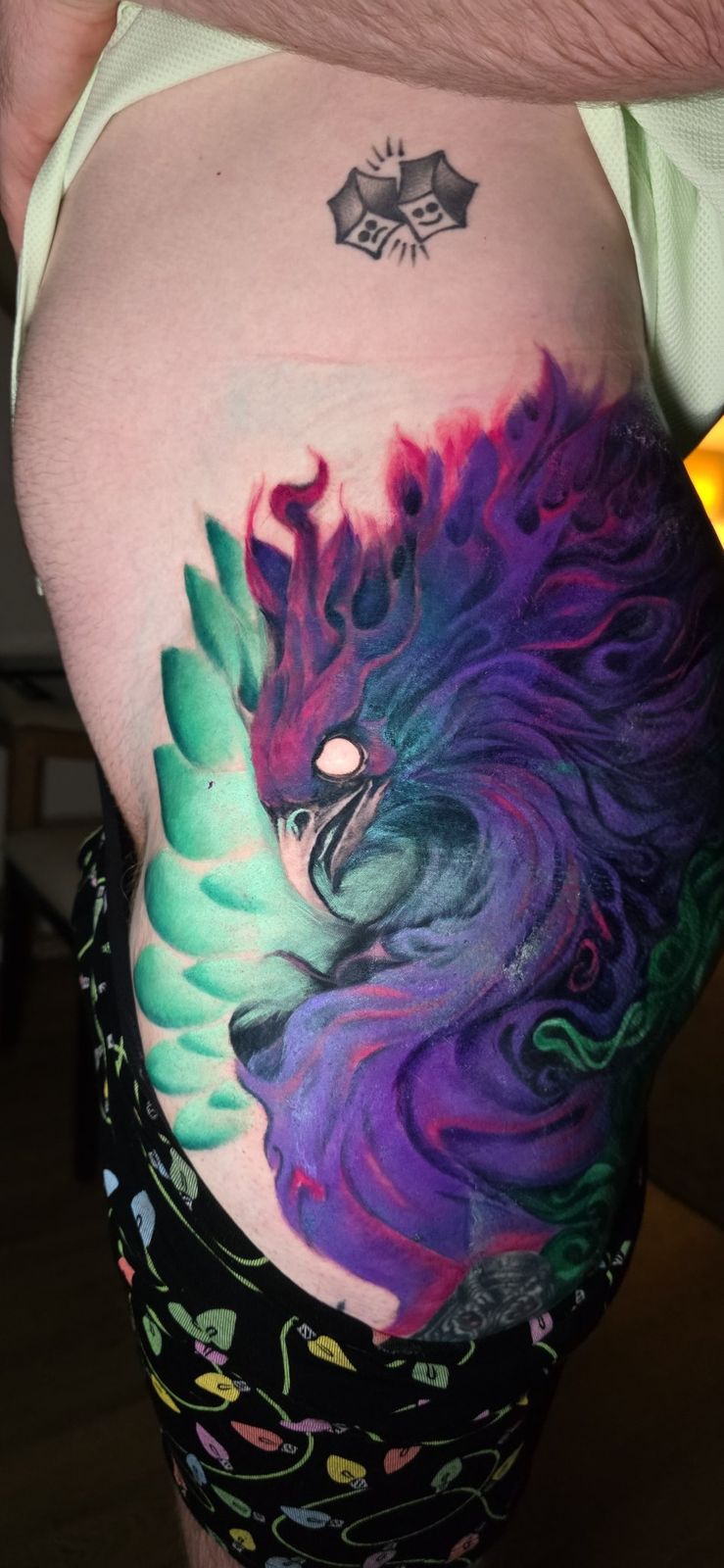 Front view of a large colorful phoenix tattoo across the thigh